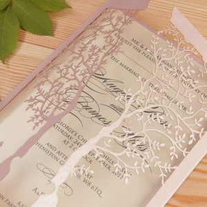 May include: A laser-cut wedding invitation with a pink and white tree design. The invitation features the text "Request the pleasure of the company of" and "The marriage of their daughter".