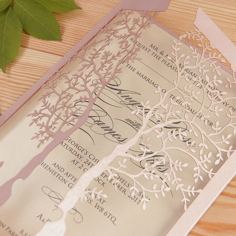 May include: A laser-cut wedding invitation with a pink and white tree design. The invitation features the text "Request the pleasure of the company of" and "The marriage of their daughter".