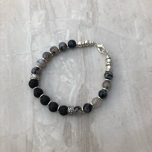 Puede incluir: Pulsera de cuentas negras y grises con detalles plateados. La pulsera presenta cuentas de lava, cuentas de ágata y cuentas espaciadoras plateadas.