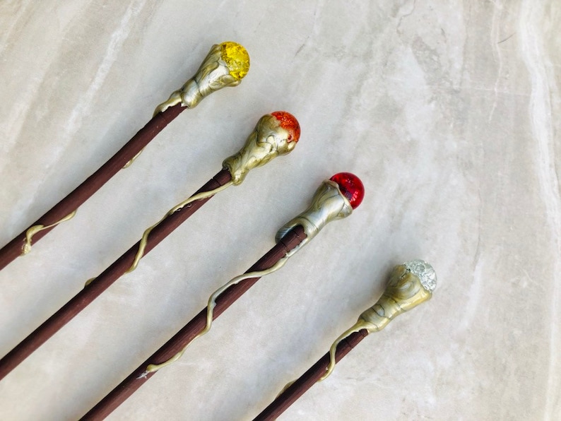 May include: Four wooden wands with different colored glass orbs on the ends. The orbs are yellow, orange, red, and clear.