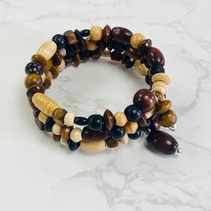 May include: A multi-strand wooden bracelet with brown, black, and natural wood beads. The bracelet is made of multiple strands of beads that are woven together.