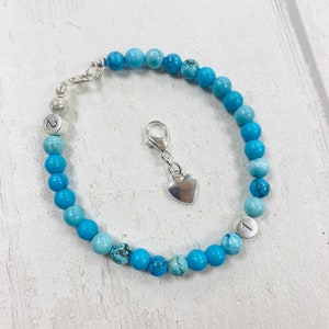 May include: A turquoise blue beaded bracelet with silver accents. The bracelet has a heart charm and two silver beads with the numbers "1" and "2" on them.