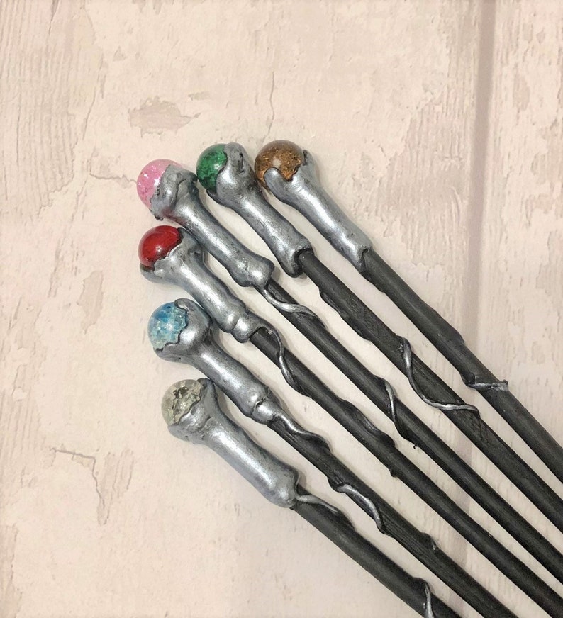 May include: A set of six silver and black wands with different colored gemstone tips. The tips are pink, green, brown, red, blue, and white.