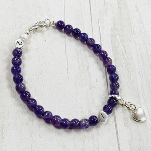 May include: Amethyst beaded bracelet with silver clasp and heart charm. The bracelet has two silver beads with the numbers "1" and "2" on them.