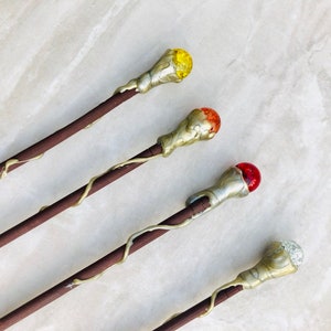 May include: Four wooden wands with different colored glass tips. The tips are yellow, orange, red, and clear.