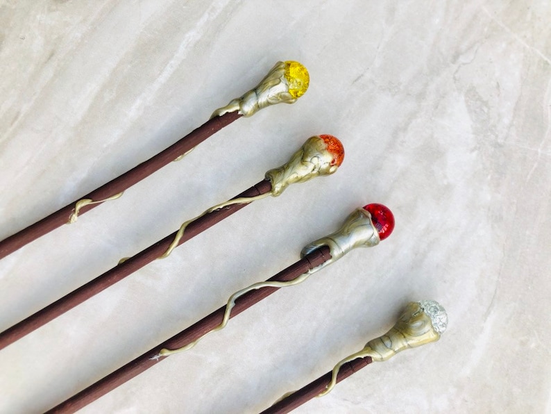 May include: Four wooden wands with different colored glass tips. The tips are yellow, orange, red, and clear.