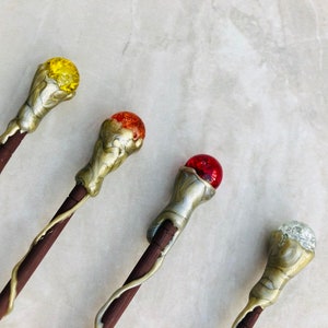May include: Four decorative wands with different colored glass orbs on top. The wands are made of wood and have a metallic finish. The orbs are yellow, orange, red, and clear.