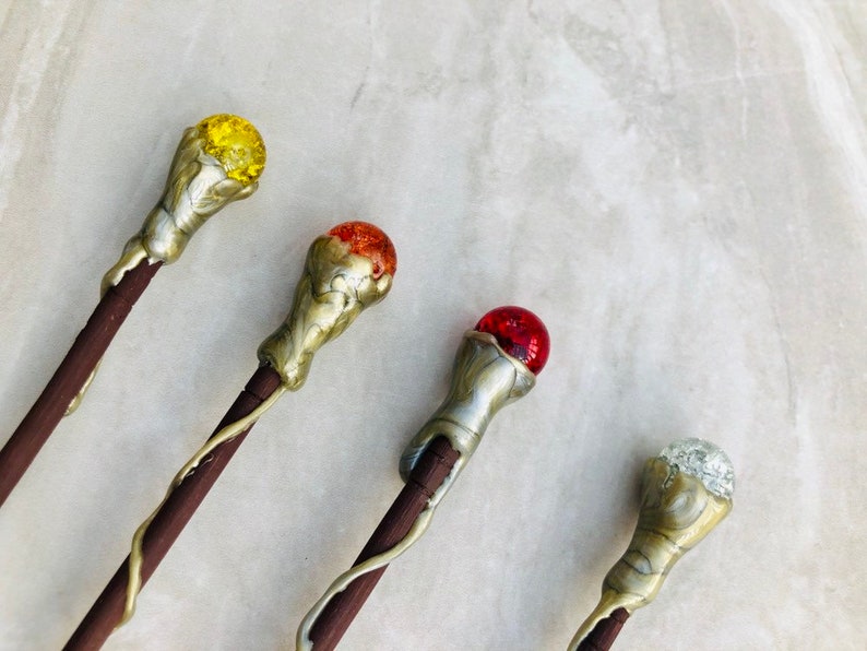 May include: Four decorative wands with different colored glass orbs on top. The wands are made of wood and have a metallic finish. The orbs are yellow, orange, red, and clear.