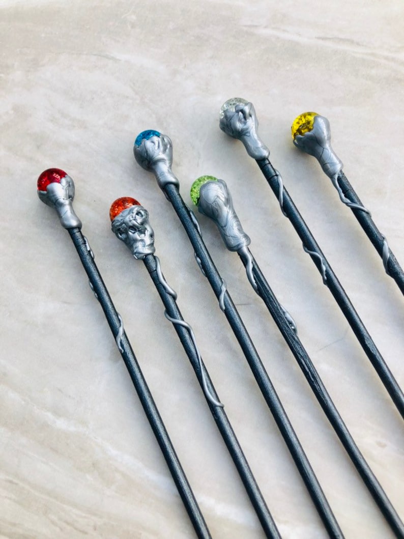 May include: Seven silver wands with different colored gemstone tips. The wands have a silver vine design and are arranged in a row.