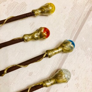 May include: Four decorative wands with different colored glass orbs on the ends. The wands are made of wood and have a gold-colored finish. The orbs are yellow, red, blue, and clear with glitter.