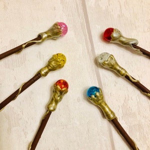 May include: Six decorative wands with different colored glass orbs on the ends. The wands are made of brown wood with a gold-colored metal tip. The orbs are pink, red, yellow, orange, blue, and clear.