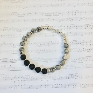 May include: A bracelet with black lava rock and grey and white agate beads. The bracelet has silver metal accents and a clasp.