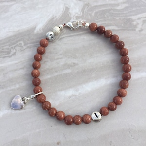 May include: A brown beaded bracelet with silver charms, including a heart charm and two charms with the numbers "1" and "2" engraved on them.