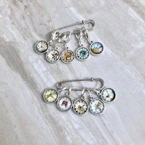 May include: Set of 10 silver stitch markers with clock face designs. The markers are attached to a safety pin.