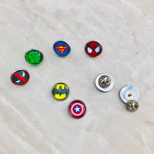 May include: A set of eight superhero themed pins. The pins feature Superman, Spiderman, Hulk, Deadpool, Batman, Captain America, and two blank pins.