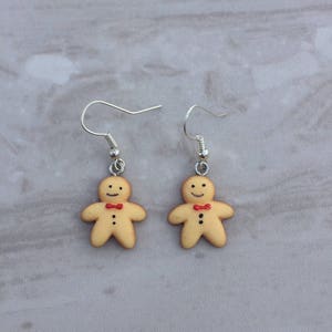 May include: A pair of gingerbread man earrings with red bow ties. The earrings are made of polymer clay and have silver hooks.