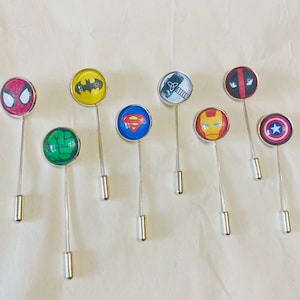 May include: A set of ten superhero themed lapel pins with silver pins. The pins feature characters such as Superman, Batman, Spiderman, Iron Man, Captain America, and Hulk.