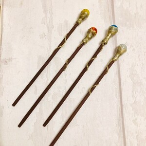 May include: Four wooden wands with gold accents and colorful gemstone tips. The tips are yellow, orange, blue, and clear.
