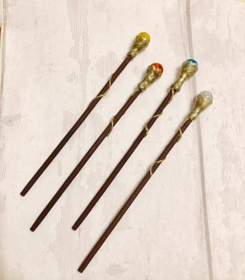 May include: Four wooden wands with gold accents and colorful gemstone tips. The tips are yellow, orange, blue, and clear.