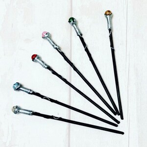 May include: Six black wands with silver tips and colorful gemstone accents. The gemstones are green, pink, red, blue, gold, and a light brown color.