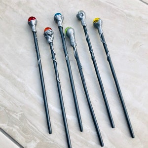 May include: Seven silver wands with different colored gemstone tops. The wands are black with silver accents and have a vine-like design.