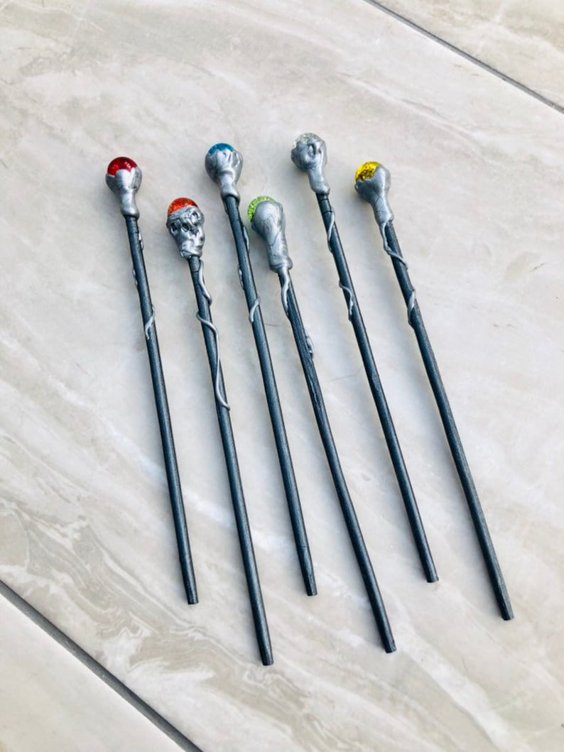 May include: Seven silver wands with different colored gemstone tops. The wands are black with silver accents and have a vine-like design.