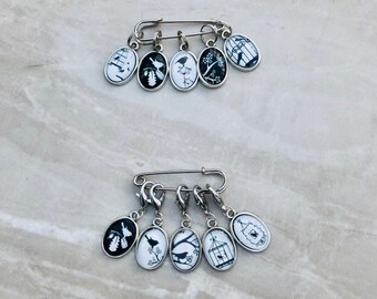 May include: Set of six silver stitch markers with black and white bird and cage designs. The markers are attached to a silver safety pin.