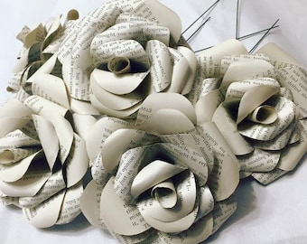 May include: A bouquet of six paper roses made from the pages of old books. The roses are a light cream color and have a vintage aesthetic.
