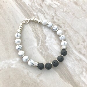 Puede incluir: Pulsera de cuentas con cuentas blancas y negras estampadas, intercaladas con cuentas y espaciadores de metal plateado. La pulsera también incluye cuentas de piedra de lava negra y un cierre plateado.