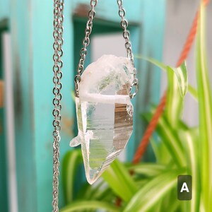 Large Clear Quartz raw crystal necklace with a stainless steel chain shown dangling with plants and crystals in the background.