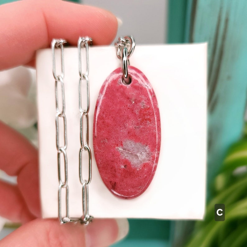 Natural pink polished Thulite stone necklace with silver tone stainless steel paperclip chain shown against a white background with plants.