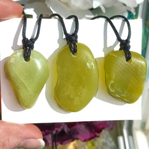 Vibrant green freeform shaped natural Washington Serpentine crystal necklaces with adjustable black cords shown in hand against a white background with flowers and plants.