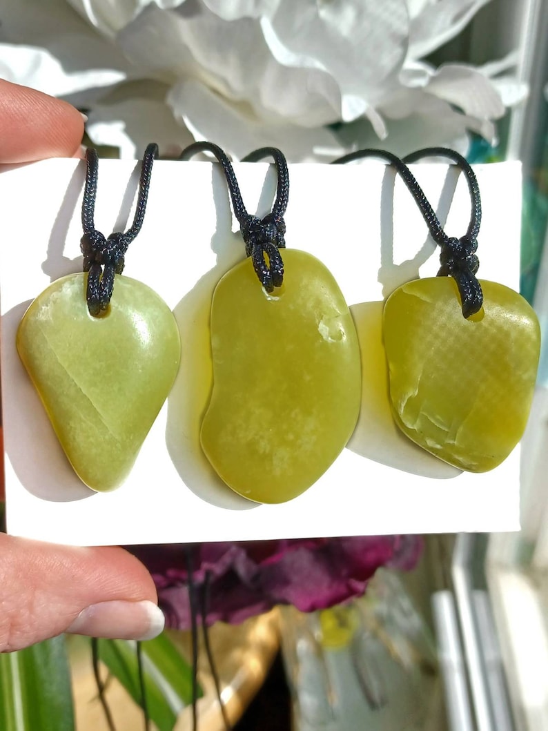 Vibrant green freeform shaped natural Washington Serpentine crystal necklaces with adjustable black cords shown in hand against a white background with flowers and plants.