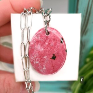 Natural pink polished Thulite stone necklace with silver tone stainless steel paperclip chain shown against a white background with plants.