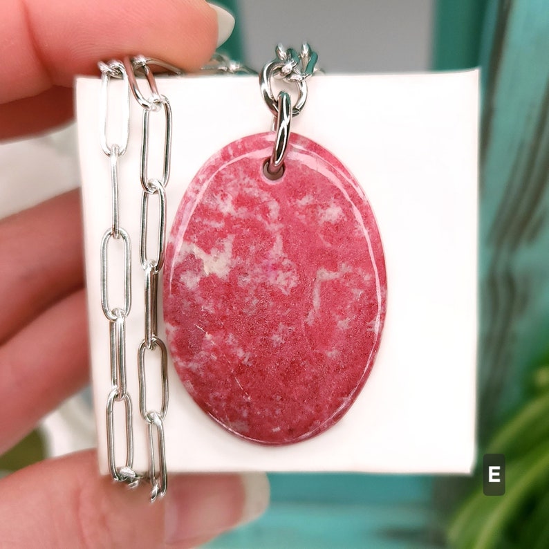 Natural pink polished Thulite stone necklace with silver tone stainless steel paperclip chain shown against a white background with plants.