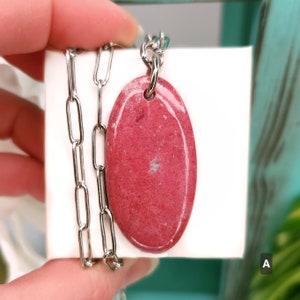 Natural pink polished Thulite stone necklace with silver tone stainless steel paperclip chain shown against a white background with plants.