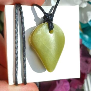 Vibrant green freeform shaped natural Washington Serpentine crystal necklace with an adjustable black cord shown in hand against a white background with flowers and plants.