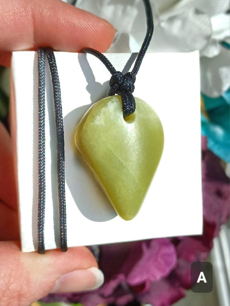 Vibrant green freeform shaped natural Washington Serpentine crystal necklace with an adjustable black cord shown in hand against a white background with flowers and plants.