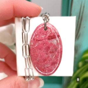 Natural pink polished Thulite stone necklace with silver tone stainless steel paperclip chain shown against a white background with plants.
