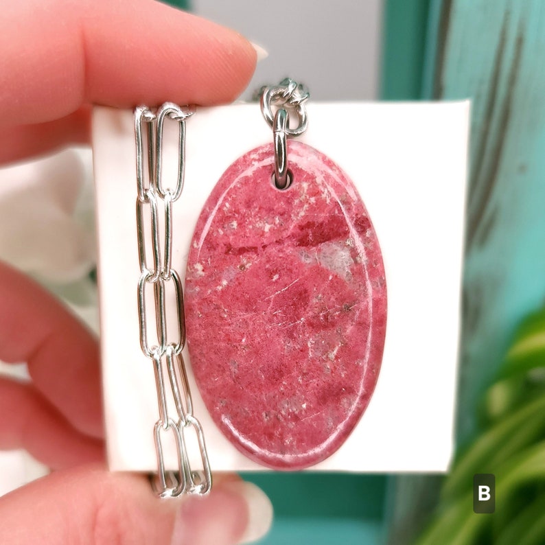 Natural pink polished Thulite stone necklace with silver tone stainless steel paperclip chain shown against a white background with plants.