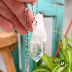 Large Clear Quartz raw crystal necklace with a stainless steel chain shown dangling with plants and crystals in the background.