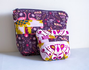 May include: Two purple fabric pouches with floral and bird patterns. The larger pouch has a zipper closure and the smaller pouch is a simple rectangle.