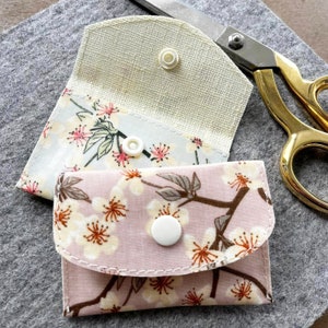 Può includere: Due piccole pochette in tessuto con motivi floreali e bottoni bianchi. Le pochette sono realizzate in un tessuto morbido e testurizzato e hanno un design semplice ed elegante.