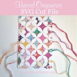 Puede incluir: Una tarjeta blanca con un patrón floral colorido y múltiples agujeros para enhebrar. La tarjeta está etiquetada como "Thread Organiser SVG Cut File" y tiene el sitio web "www.lorelei Jayne.com" impreso en la parte inferior. Varios hilos de colores se enhebran a través de los agujeros.