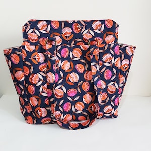 Könnte beinhalten: Eine große dunkelblaue Tragetasche mit zwei Henkeln oben und einem Blumendruck mit roten, orangefarbenen und pinkfarbenen Blumen auf dunkelblauem Hintergrund.