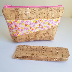 May include: A cork and fabric zipped pouch with a pink zipper and a pink and yellow floral print. The pouch is sitting on a white surface next to a smaller cork pouch.