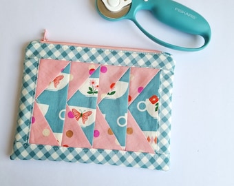 Puede incluir: Una bolsa de cremallera de tela de patchwork rosa y azul con un borde a cuadros. La bolsa presenta un patrón de tazas de té y mariposas.