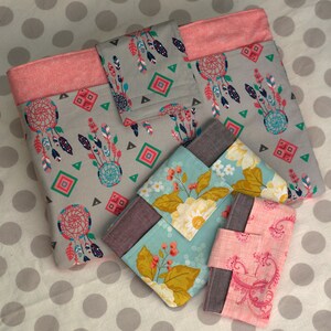 May include: Four fabric pouches with different patterns. The largest pouch is gray with a pink border and features a dreamcatcher design. The other pouches are smaller and feature floral and paisley patterns.