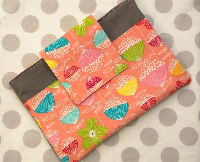 Puede incluir: Una funda para port&aacute;til de tela gris y melocot&oacute;n con un patr&oacute;n floral. La funda tiene un bolsillo m&aacute;s peque&ntilde;o en la parte delantera.