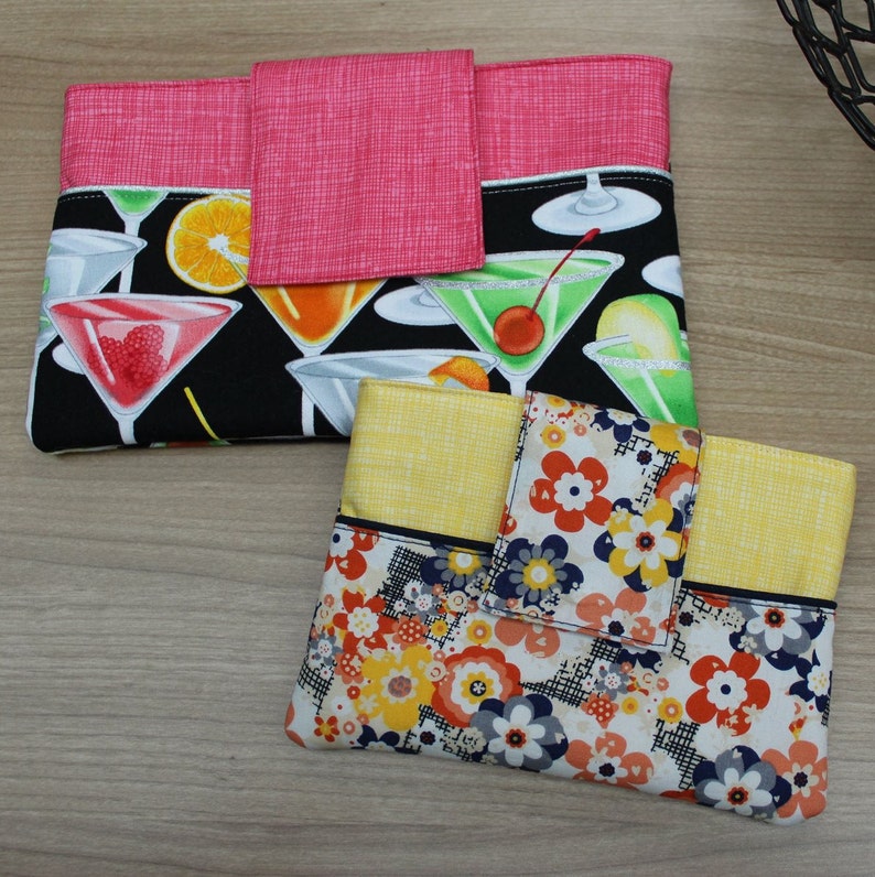 May include: Two fabric pouches with a flap closure. The pouch on the left has a black background with a colorful cocktail print. The pouch on the right has a yellow background with a floral print.